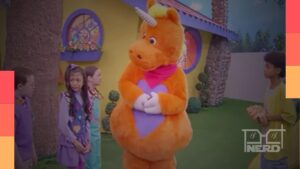 Cena do filme Buddy com um unicórnio laranja assassino em clima de programa infantil que virou terror